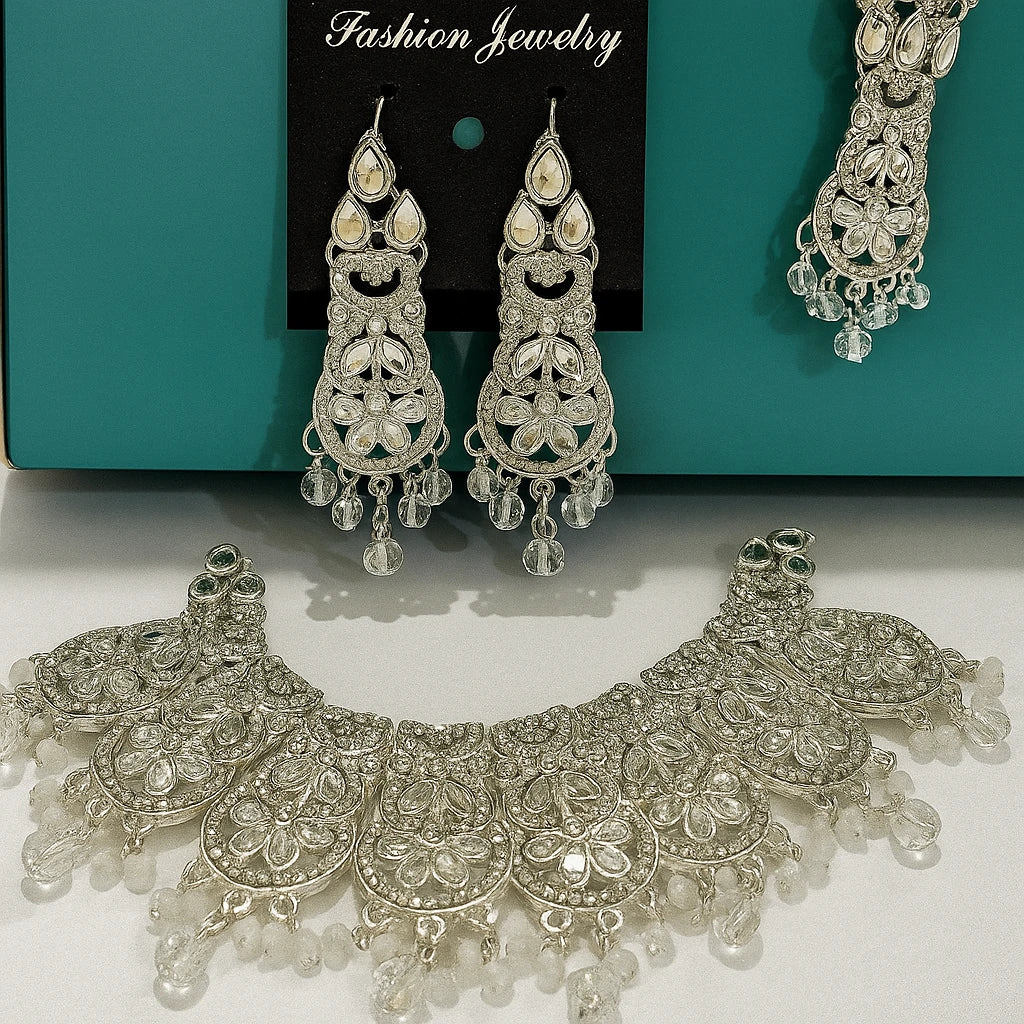 Silver jewelry set with necklace and earrings on a white surface with teal background