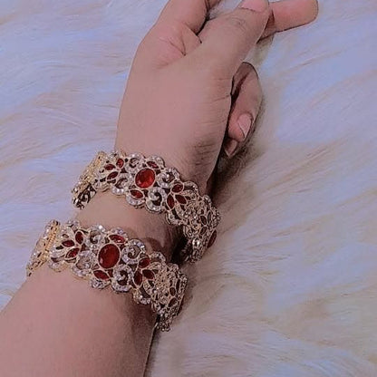 Hand wearing two ornate bracelets with red stones on a light background